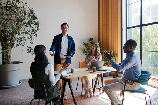 Diverse business team collaborating and celebrating success during an office meeting, colleagues applauding a male presenter in a modern workspace