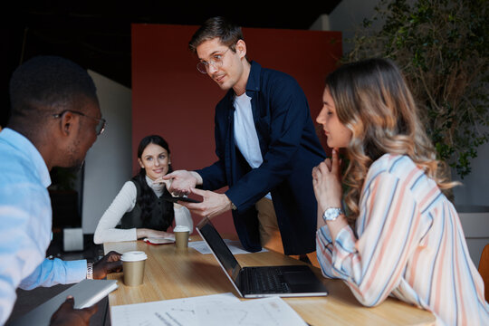 Diverse business professionals conducting a meeting. Collaborating around a laptop and documents on a wooden table. Discussing strategy and ideas for a startup