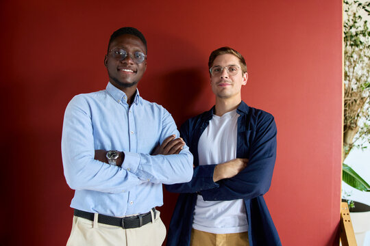 Diverse business professionals standing with arms crossed, smiling confidently in an office setting, representing teamwork, partnership, and successful collaboration