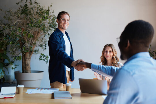 Business professionals shaking hands, completing a successful deal, celebrating teamwork and collaboration during a corporate meeting in a modern office