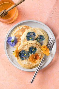 Top view of homemade pancakes with embedded edible pansy flowers and honey butter