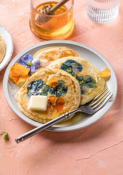 Top view of homemade pancakes with embedded edible pansy flowers and honey butter