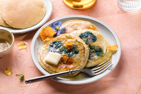 Top view of homemade pancakes with embedded edible pansy flowers and honey butter