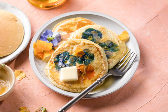 Top view of homemade pancakes with embedded edible pansy flowers and honey butter