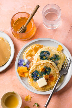 Top view of homemade pancakes with embedded edible pansy flowers and honey butter