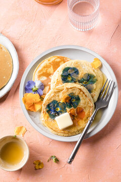 Top view of homemade pancakes with embedded edible pansy flowers and honey butter