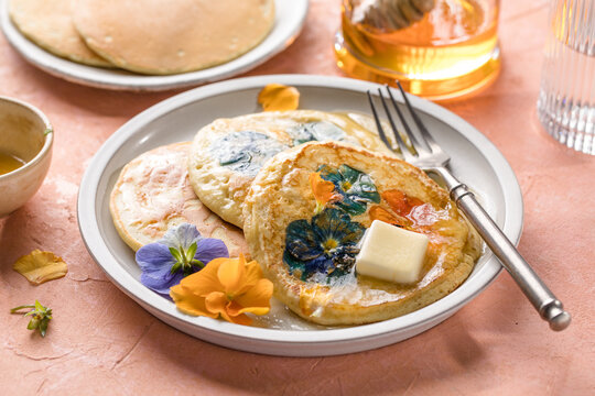 Top view of homemade pancakes with embedded edible pansy flowers and honey butter