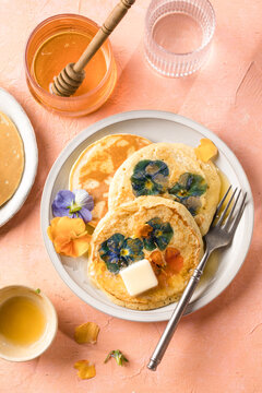 Top view of homemade pancakes with embedded edible pansy flowers and honey butter