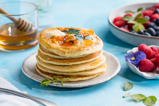 Top view of homemade pancakes with embedded edible pansy flowers and honey butter