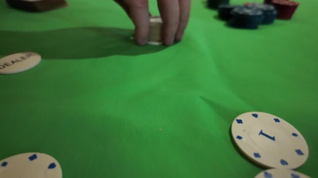 A close up view captures a hand deftly shuffle and stack poker chips on a vibrant green table. The mood is focused and strategic, set in a casino or game room environment. This footage is perfect for