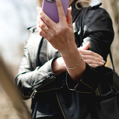 Fototapeta premium Busy modern woman with sunglasses and a black leather jacker on her mobile device outside on a cool fall afternoon.