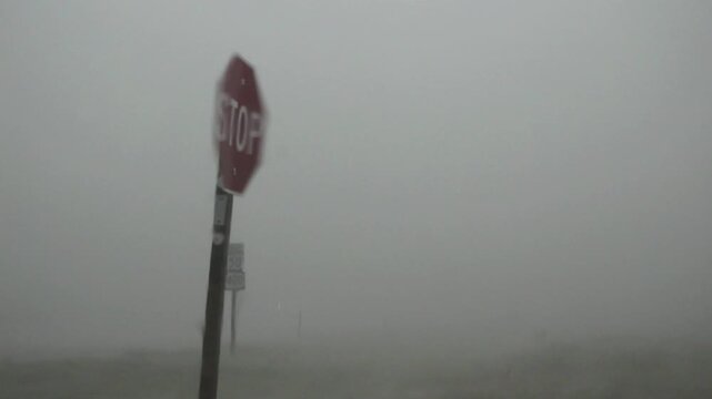 A stop sign flaps erratically in severe wind and rain produced by a dangerous storm in the great plains. 