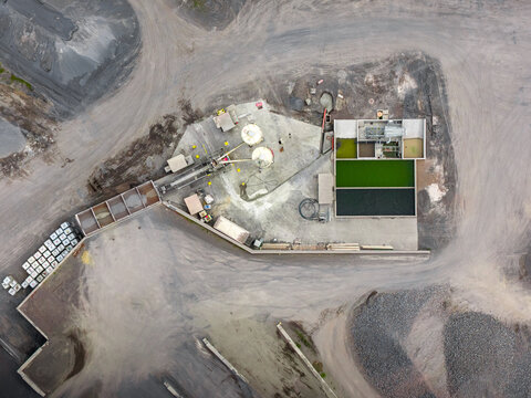 Aerial view of the Tecnovia Acores industrial facility, showing concrete silos, processing equipment, storage tanks, and surrounding gravel yards in Rabo de Peixe, Acores, Portugal.
