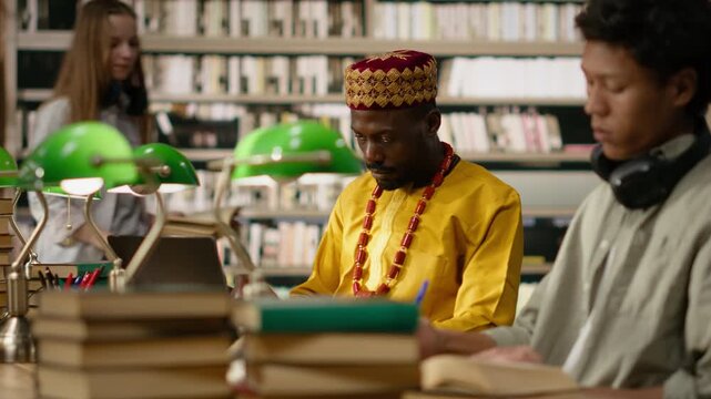 Black mature student typing on desktop monitor in library computer lab, african traditional clothing and accessories during computer class, adult at computer screen during study session.