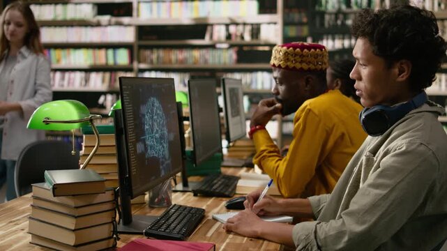 Asian student working with AI brain display on desktop monitor in library computer lab, surrounded by books stacked across wooden study table, neural network screen, for technology research.