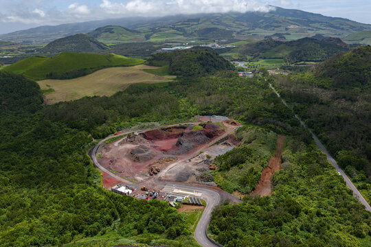 Aerial view of the Tecnovia Acores quarry site with red earth, heavy machinery, and surrounding lush green hills near Rabo de Peixe, Acores, Portugal.