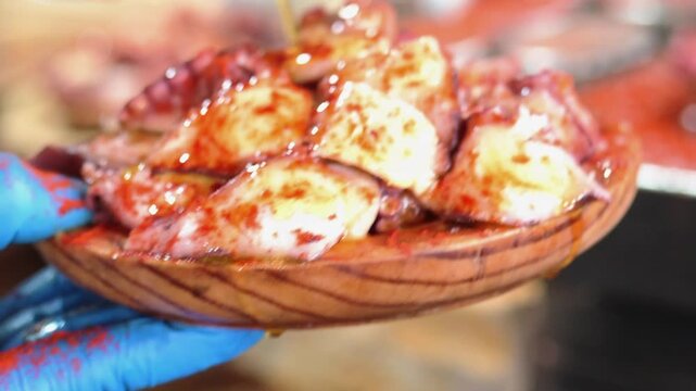 Close up of a chef pouring extra virgin olive oil over a wooden plate of galician style octopus, a traditional spanish tapa recipe