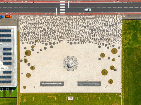 Aerial view of the public square featuring a decorative circular mosaic pattern, surrounded by green lawns and a nearby road in Ribeira Grande, Azores, Portugal.