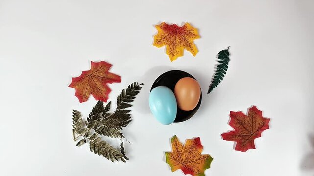 Flat lay of colorful Easter eggs with autumn maple leaves on white background