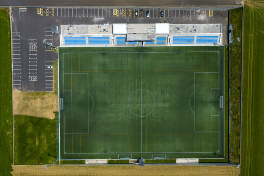 Aerial view of a football stadium with green artificial turf, white pitch markings, blue seating, and an adjacent parking lot in Rabo de Peixe, Azores, Portugal.