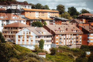 Dense residential apartment buildings with terracotta roofs on a green hillside under dramatic cloudy sky in an Asturias town © skyNext