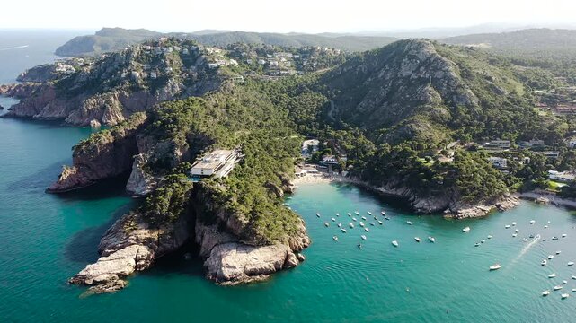 Aerial view of Aiguablava Beach, one of the most beautiful coves on the Costa Brava, featuring crystal-clear turquoise waters, rocky islets and lush Mediterranean pine forests. 