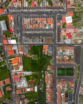 Aerial view of the residential neighborhood with orange rooftops, narrow streets, and a small soccer field in Rabo de Peixe, Azores, Portugal.
