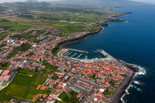 Aerial view of the coastal town with its harbor, red-tiled rooftops, and surrounding green agricultural fields in Rabo de Peixe, Azores, Portugal.