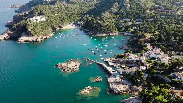 Aerial view of Aiguablava Beach, one of the most beautiful coves on the Costa Brava, featuring crystal-clear turquoise waters, rocky islets and lush Mediterranean pine forests. 
