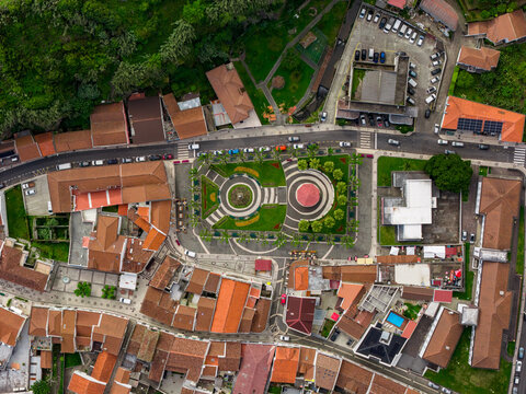 Aerial view of the town square in Povoacao with its distinctive circular garden patterns, surrounded by historic buildings with red-tiled roofs in Povoacao, Azores, Portugal.