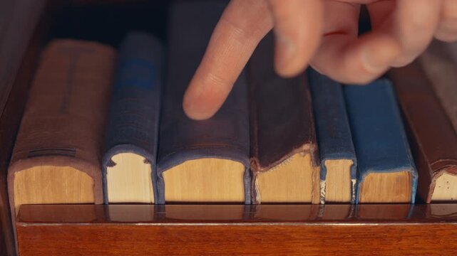 Hand Browsing Antique Books on Library Shelf Close-Up &mdash; Slow Motion | Finger Touching Worn Hardcover Spines on Wooden Shelf | Vintage Knowledge Selection Concept