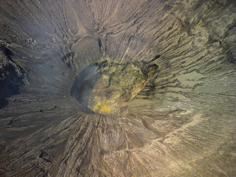Aerial view of the volcanic crater of Mount Bromo with rugged ash-covered slopes and yellow sulfur deposits in Probolinggo, East Java, Indonesia.