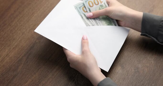 Bonus. Woman opening envelope with dollar banknotes at wooden table, closeup