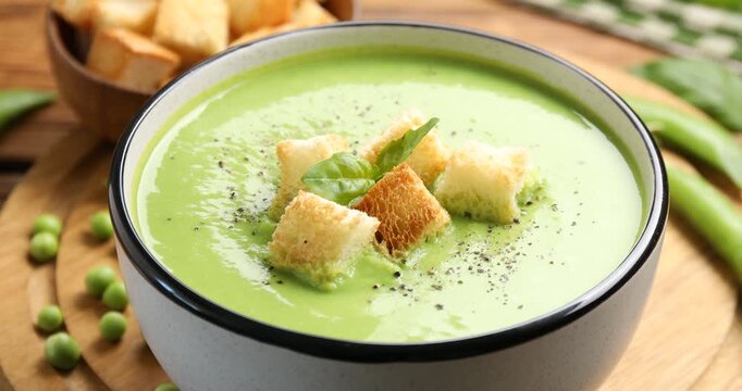 Adding spices to delicious pea cream soup with croutons at wooden table, closeup