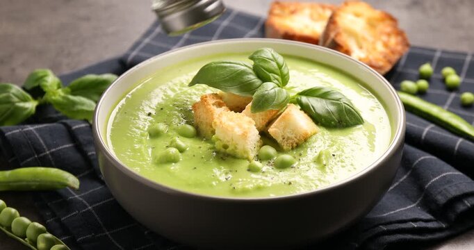 Woman adding spices to delicious pea cream soup with croutons at grey table, closeup