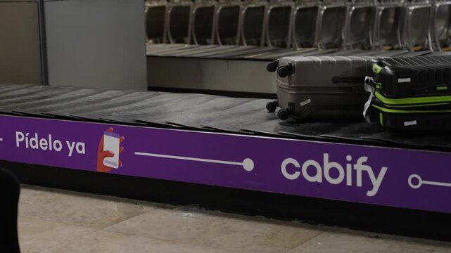 suitcases moving on baggage claim carousel with purple advertisement belt at airport
