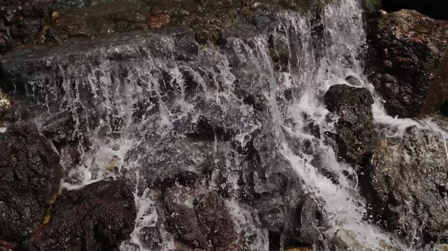 Close view of water rushing and splashing over mossy wet rocks at Katsuoji Osaka temple