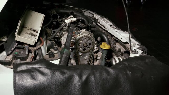 Open car engine bay showing timing chain sprocket and components in garage