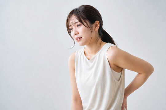 腰痛に悩み腰に手を当てる若い日本人女性 Generative AI