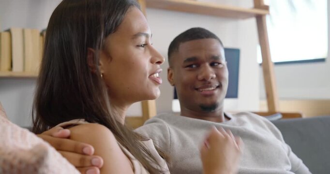 Couple on sofa at home, man leaning back speaking, holding tablet, woman listening, sharing moment