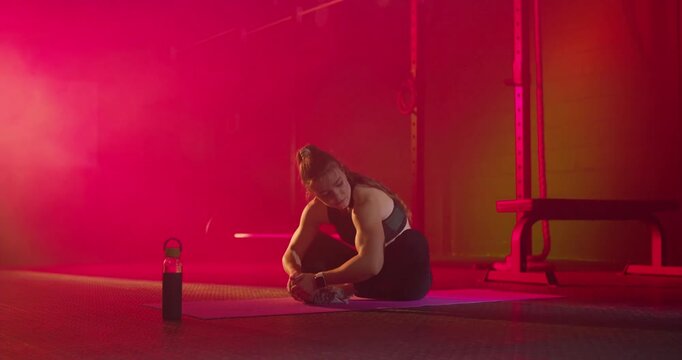 Adult female adjusting shoe warming up on purple mat in gym reaching toe holding stretch