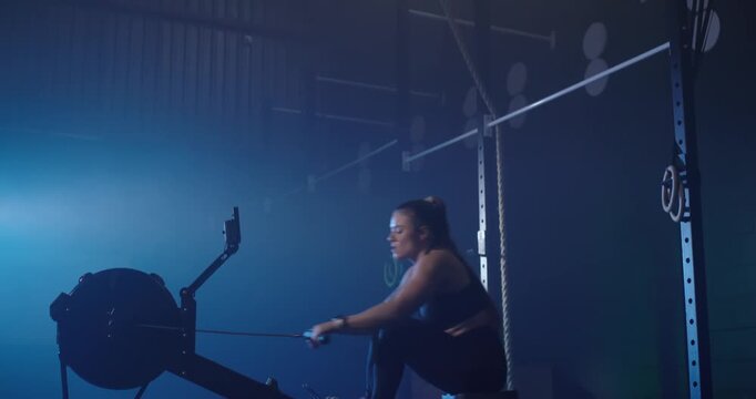 Adult female reacting to monitor prompt, strapping feet and rowing ergometer at gym rig, copy space