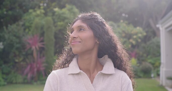 African American woman shifting gaze, turning right, smiling, laughing in garden in beige pullover