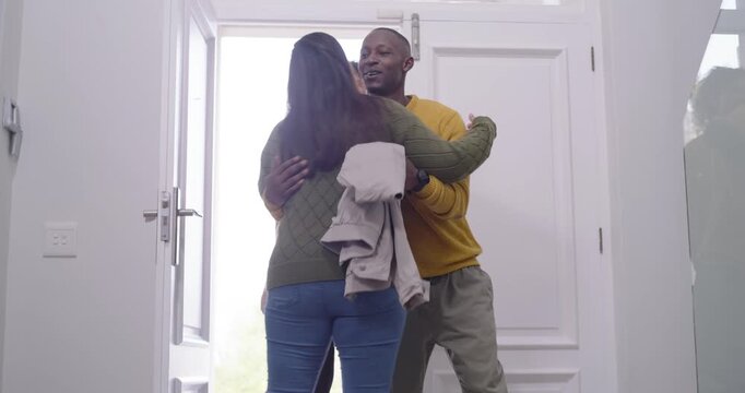 African woman in green sweater opening door welcoming friends hugging guests with jacket and purse