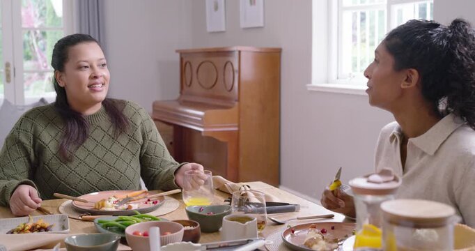 Two African American women sharing meal at home, chatting, laughing, cutting food, man joining