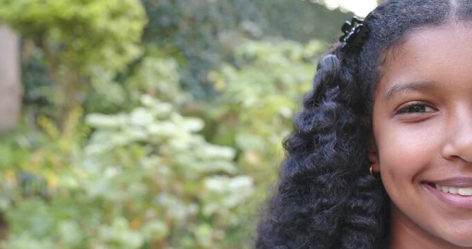 African American teenage girl shifting after half-face, smiling, showing clip in garden, copy space