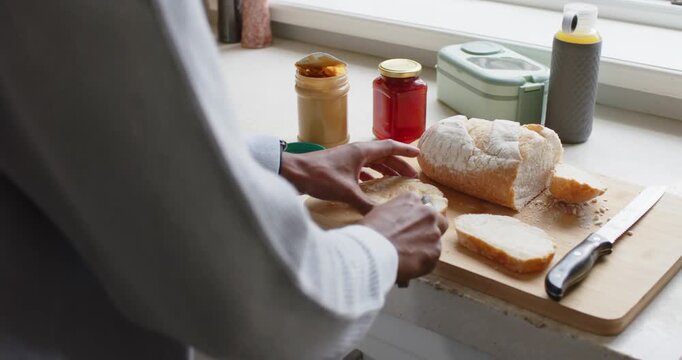African American man in knit grabbing knife scooping jam spreading on bread to eat at counter
