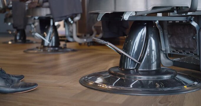 African American man in chinos pressing shoe onto barbershop pedal from left to adjust chair height
