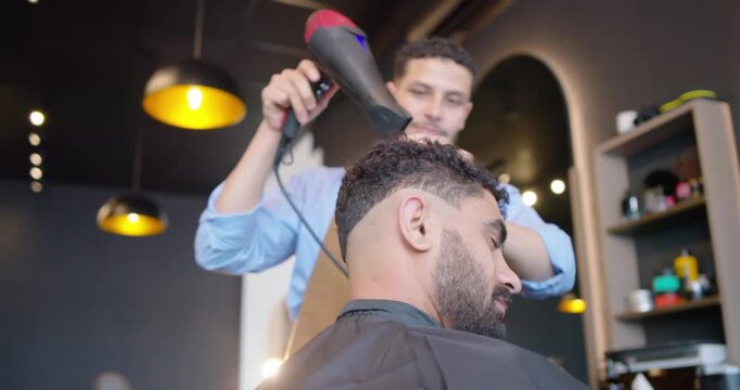 African American barber and client, barber bringing dryer shaping curls into fade at nape in shop