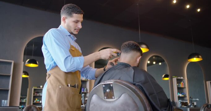 African American male barber cutting male client hair with clipper at shop on request finishing cut